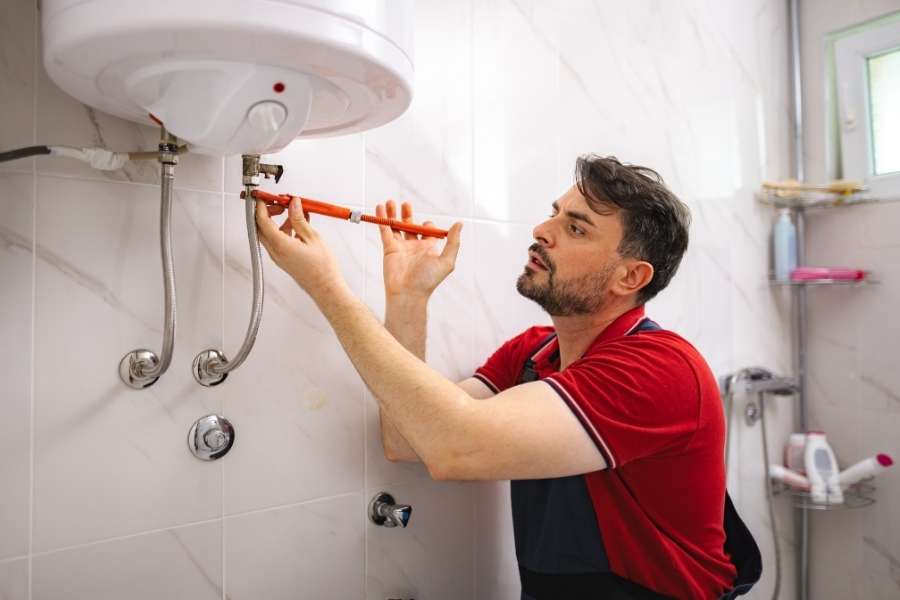 A technician uses an adjustable wrench to tighten connections on a wall-mounted water heater making strange noises.