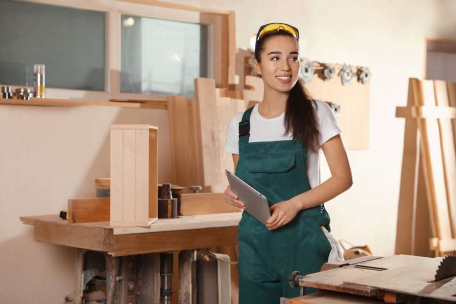 A female carpenter posing next to a professional workbench in a wood workshop.